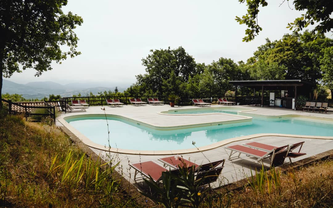 Zwembad van Camping Casa Tartufo gezien vanaf de grashelling, rode ligbedden op de voorgrond en heuvels in de nevel