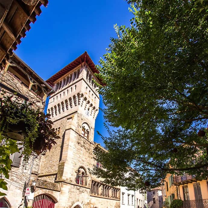 Middeleeuwse stenen toren met boogvensters en rood pannendak tegen een blauwe lucht in een stadje in de Tarn-et-Garonne