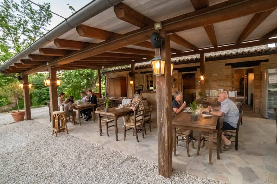Houten pilaren met brandende lantaarns op het overdekte terras, gasten aan tafel bij het vallen van de avond